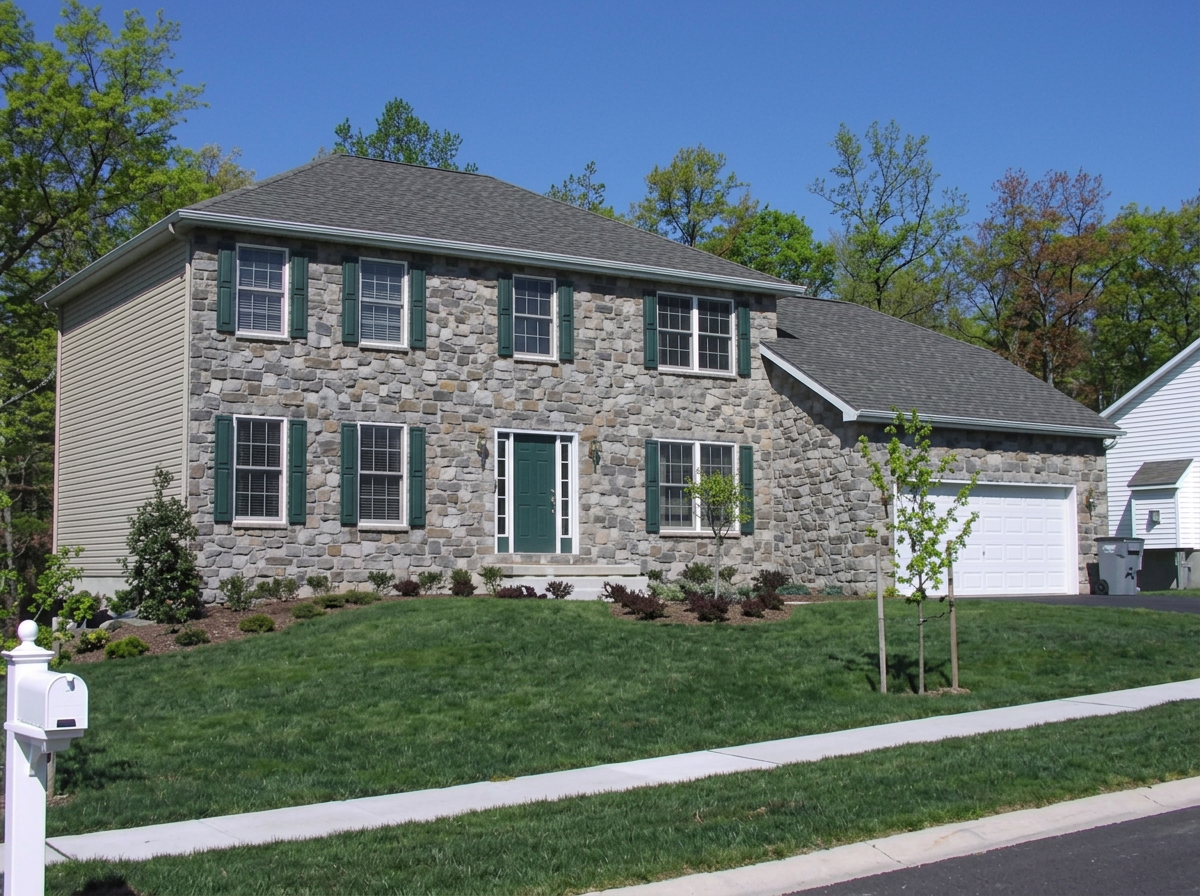 Two-story Autumn Builders colonial with full stone front and green shutters